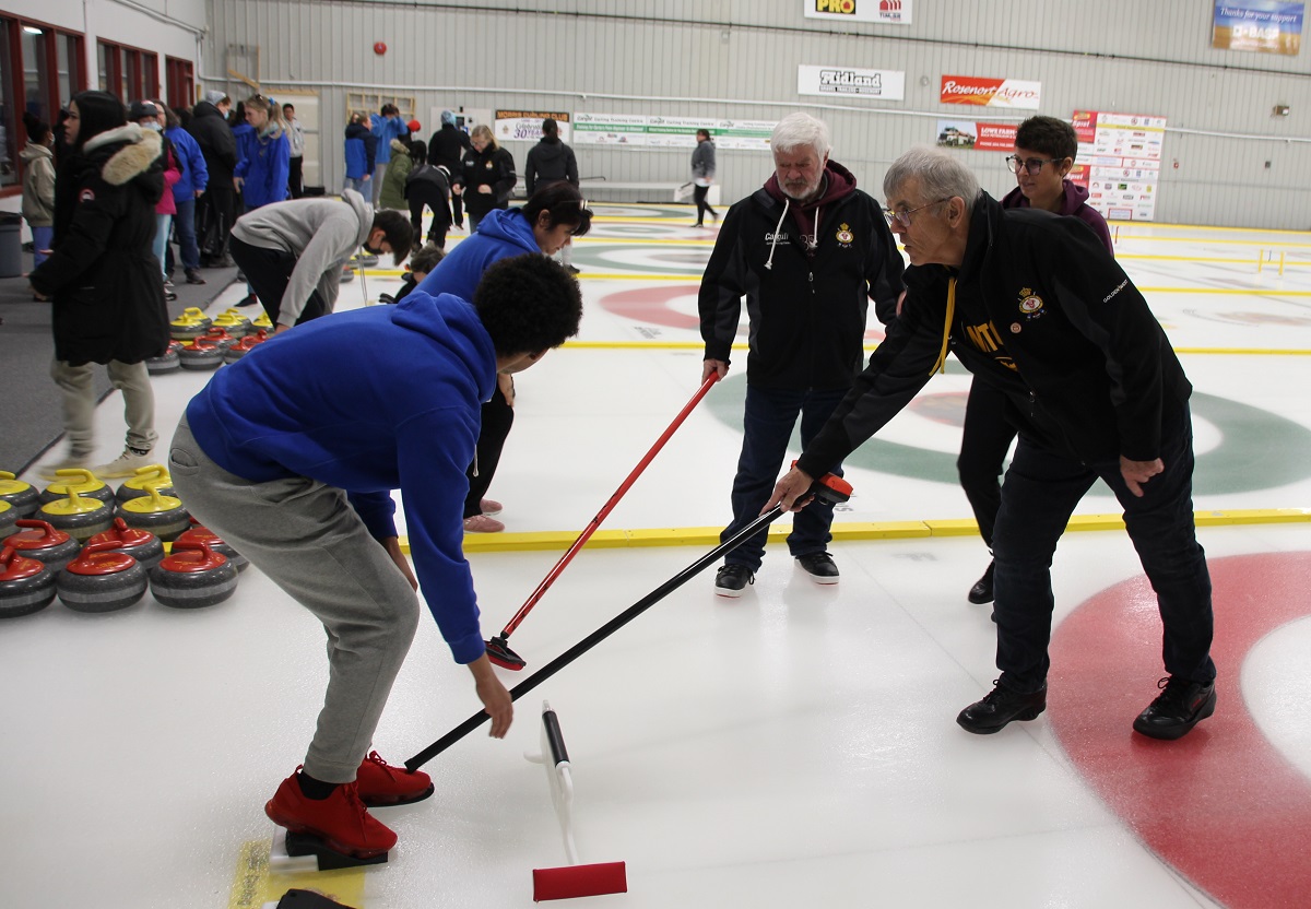 Lorne Hamblin, holding black broom, providing instruction to one of the students who participated in the workshop